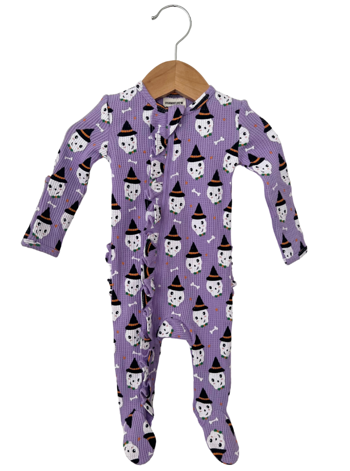 Purple infant onesie with ghost and bone pattern, featuring ruffles and a front closure, hanging on a wooden hanger.