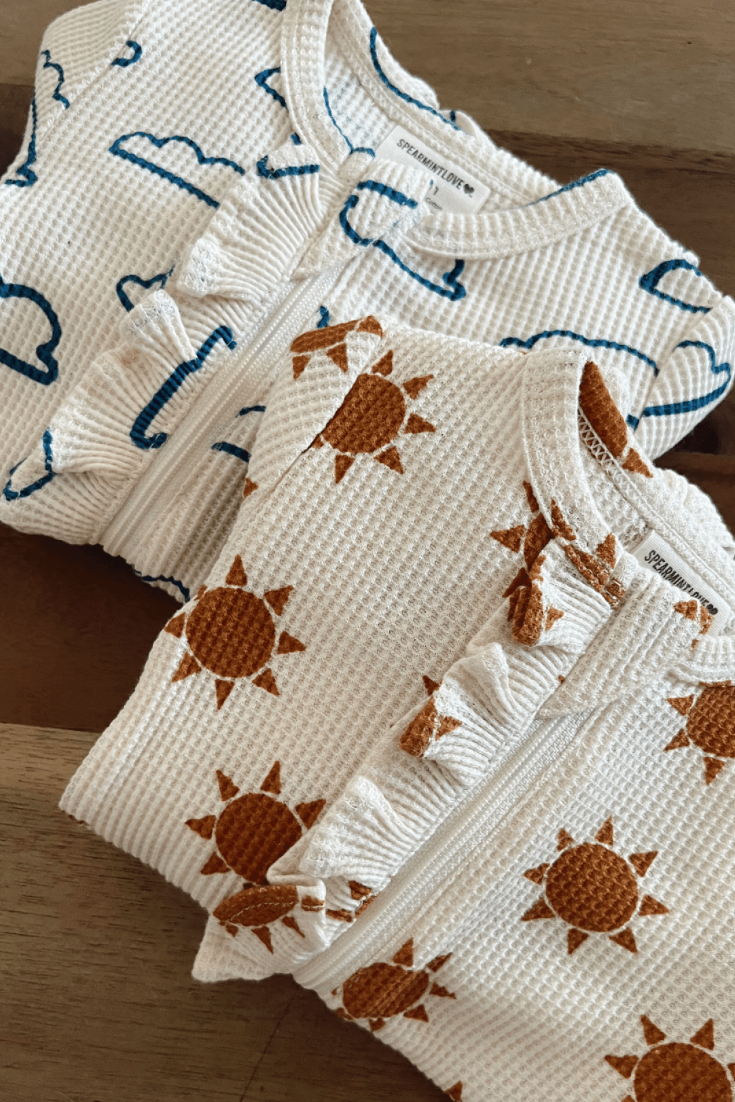 Two cozy toddler outfits with cloud and sun patterns on a wooden surface.