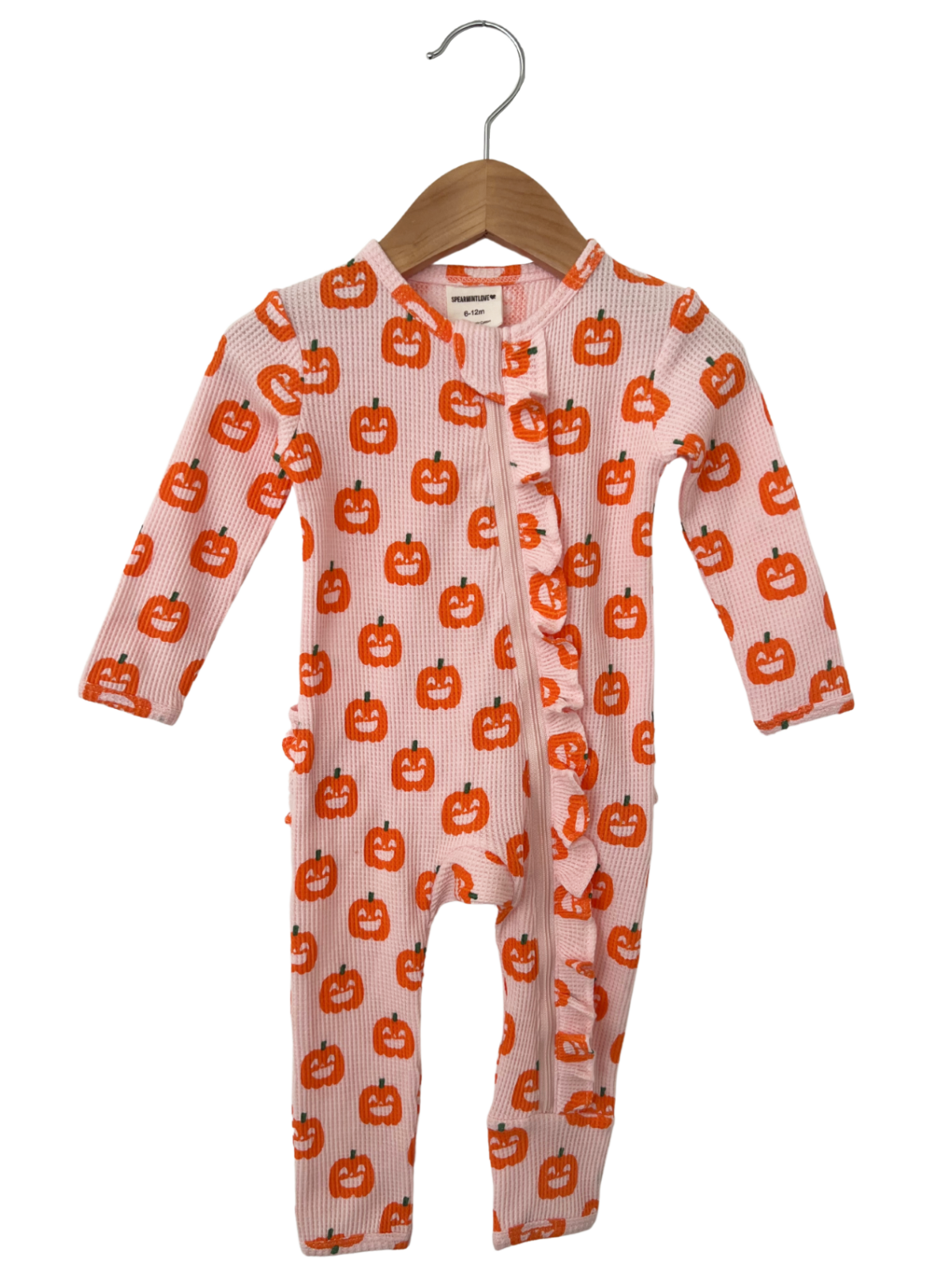 Pink baby onesie with orange pumpkin prints, featuring a ruffled front and long sleeves, hanging on a wooden hanger.