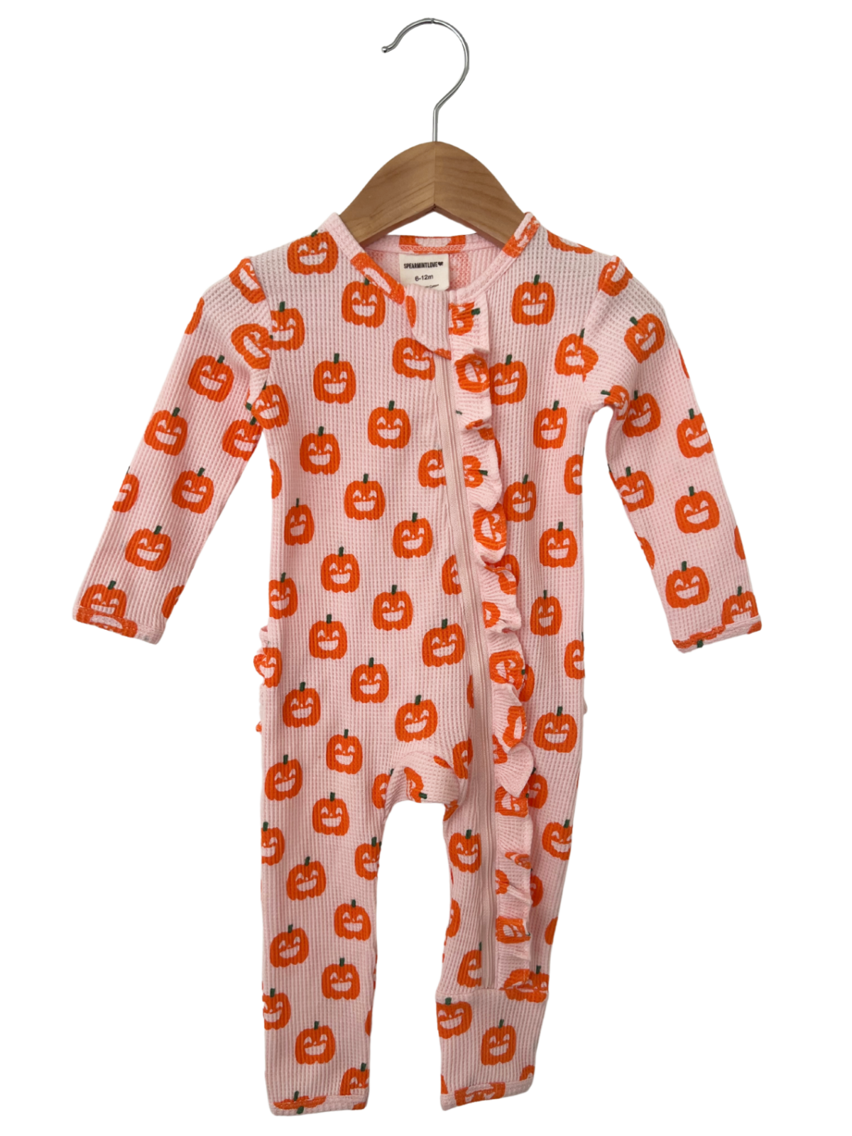 Pink baby onesie with orange pumpkin prints, featuring a ruffled front and long sleeves, hanging on a wooden hanger.