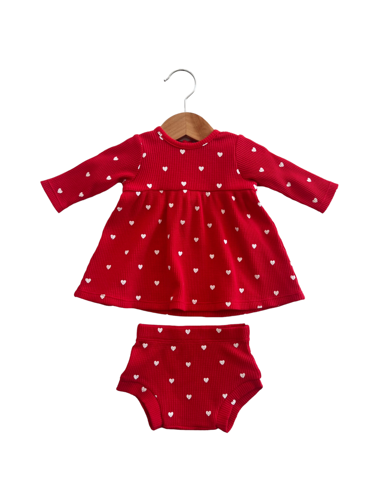 Red dress with white heart patterns and matching shorts, hanging on a wooden hanger.