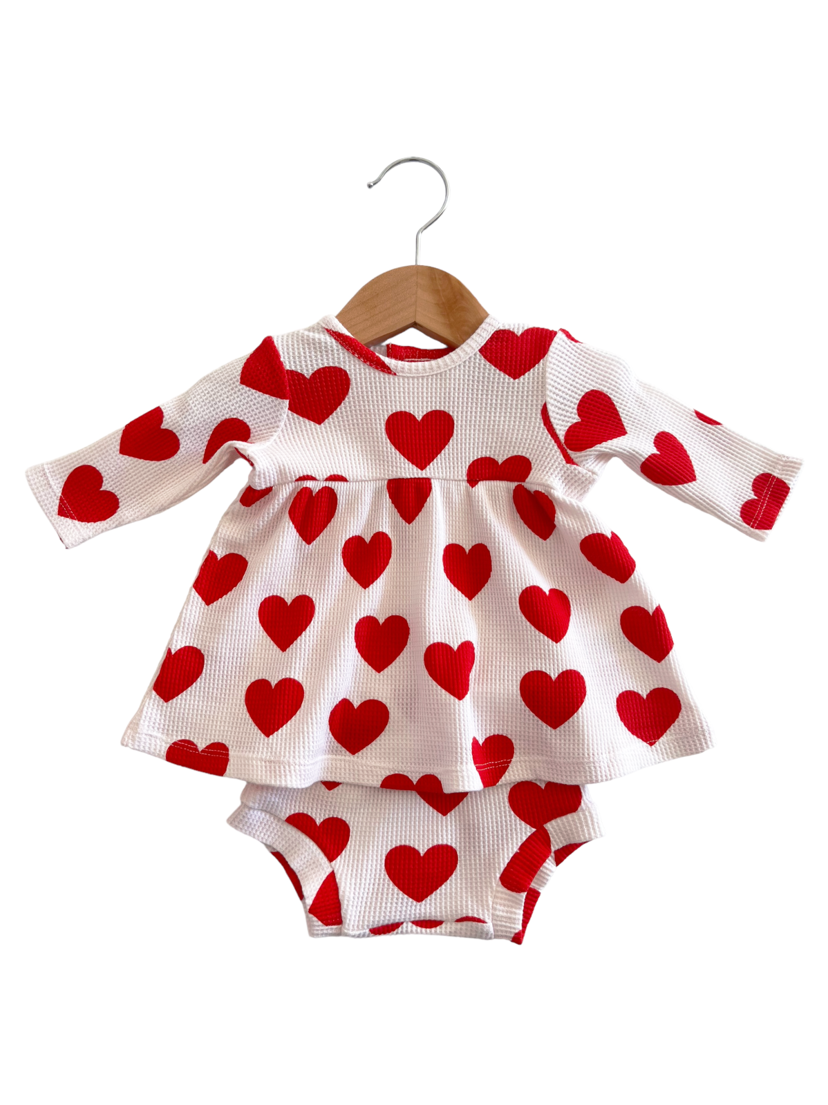 Red heart-patterned dress and matching bloomers hanging on a wooden hanger against a white background.