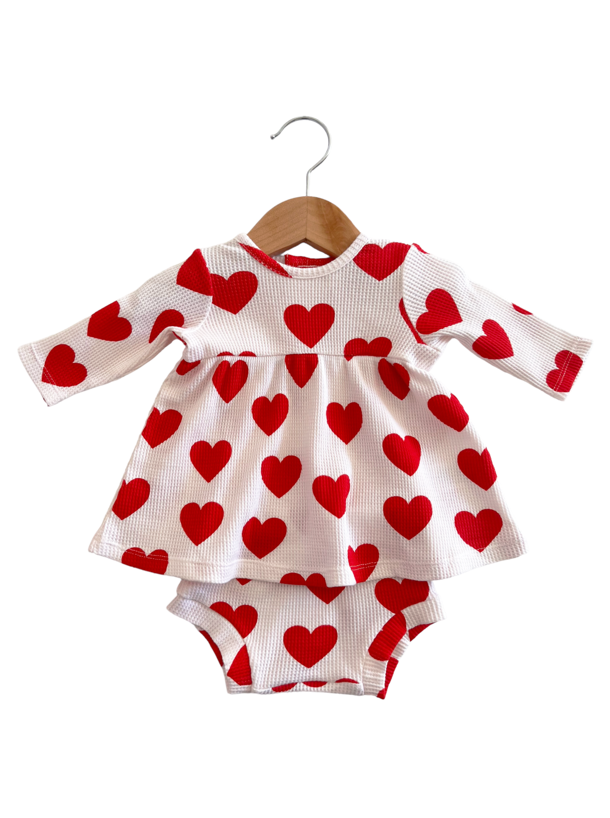 Red heart-patterned dress and matching bloomers hanging on a wooden hanger against a white background.