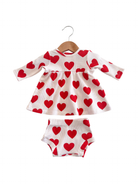 White baby dress with red heart patterns and matching shorts, hanging on a wooden hanger.