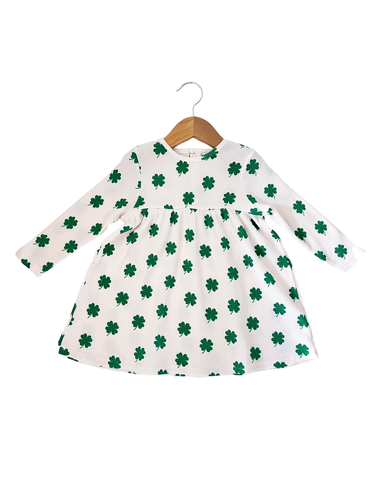 White dress with green shamrock pattern, long sleeves, displayed on a wooden hanger against a white background.