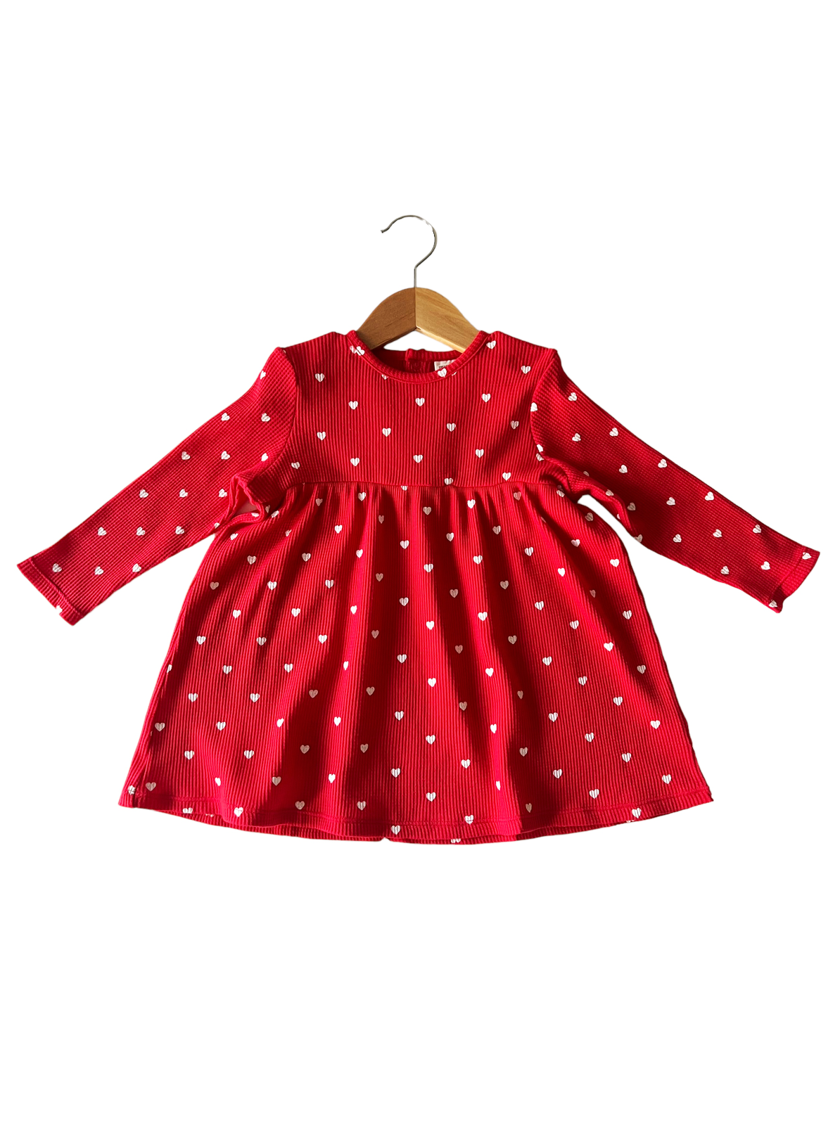 Red dress with long sleeves and white heart patterns, hanging on a wooden hanger.