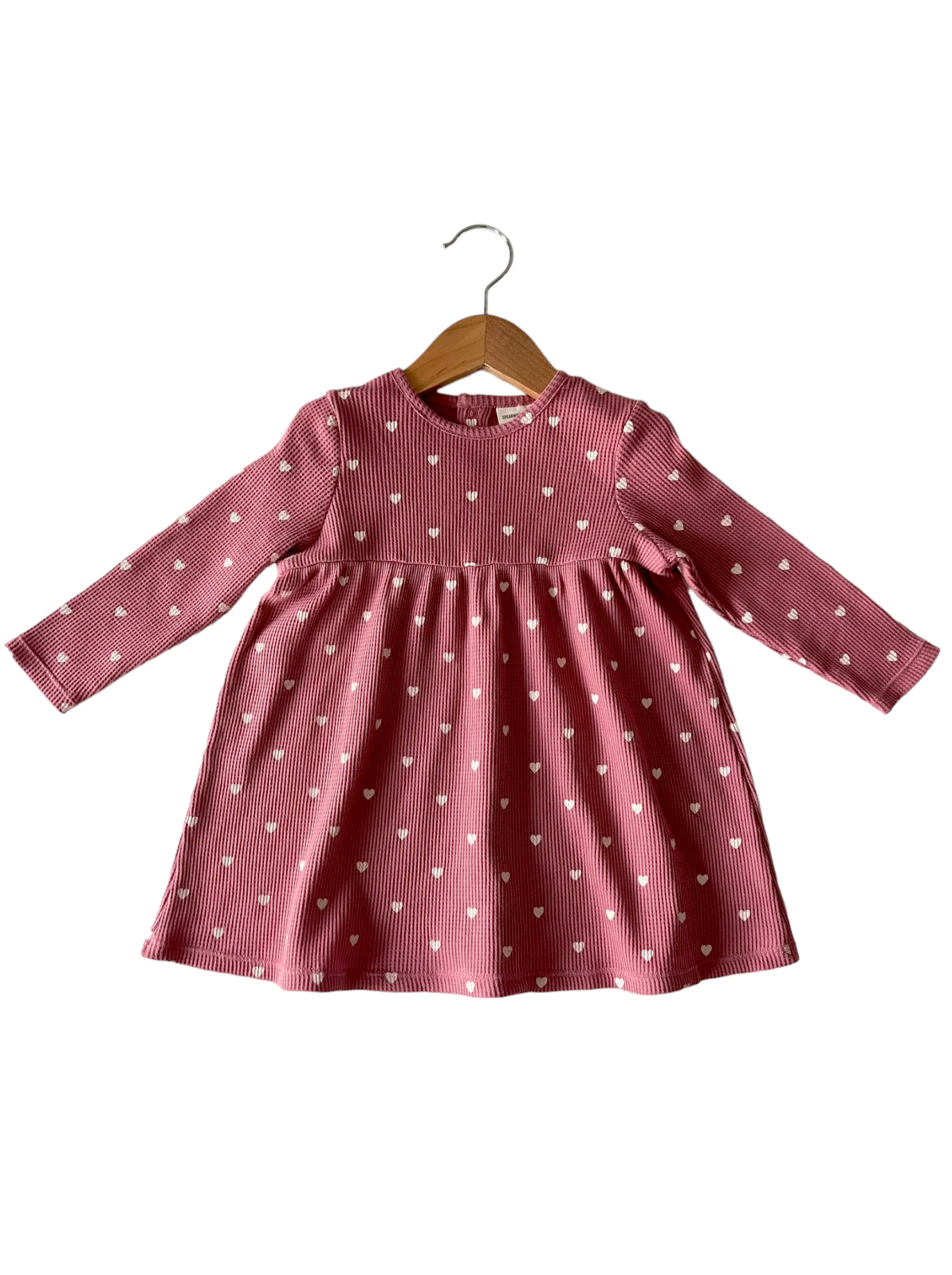 Pink long-sleeve dress with white heart patterns, displayed on a wooden hanger.