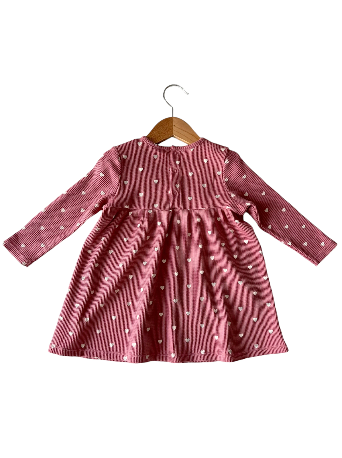 Back view of a pink striped dress with white heart patterns, hanging on a wooden hanger.