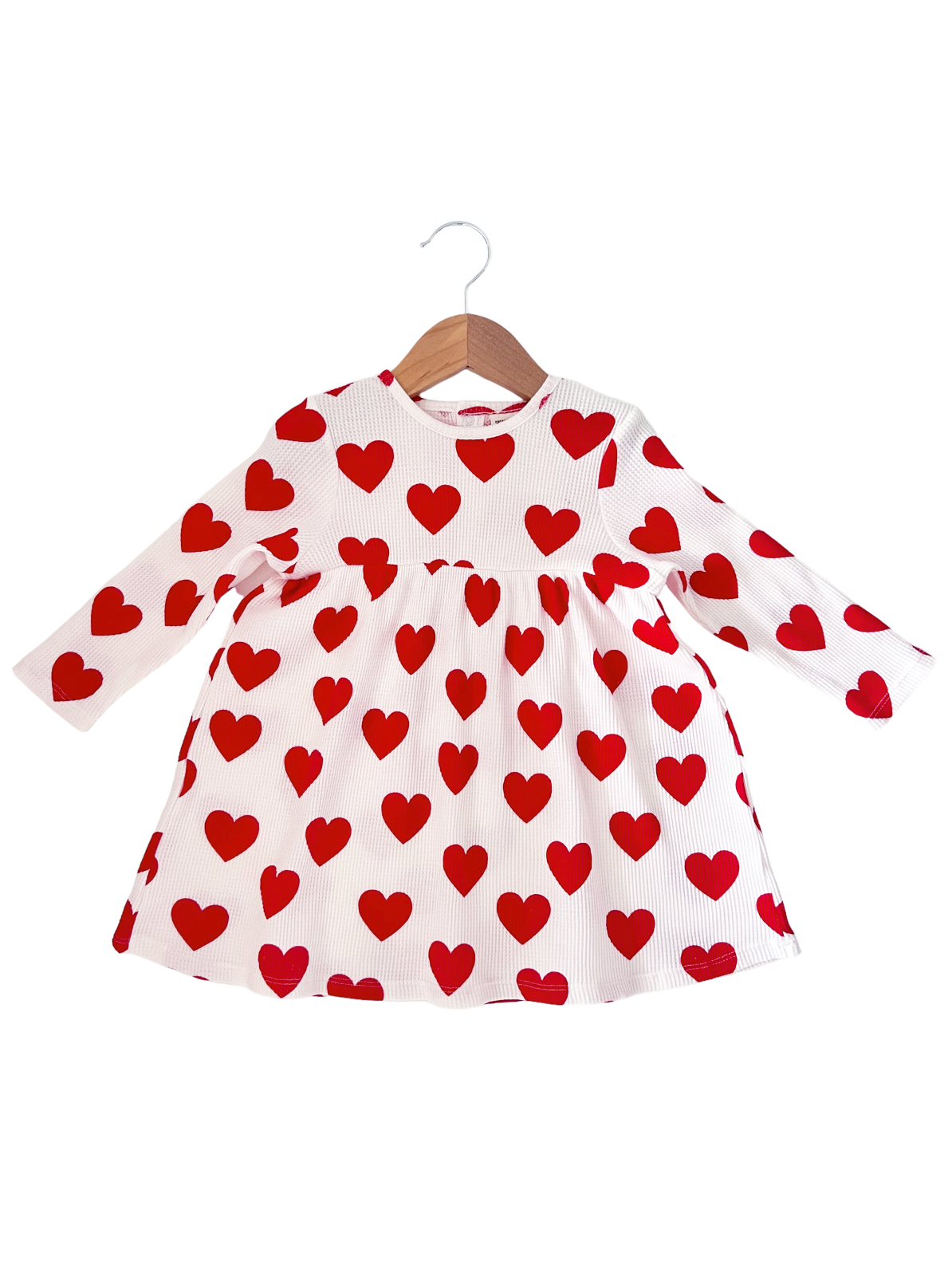 White long-sleeve dress with red heart patterns, hanging on a wooden hanger.