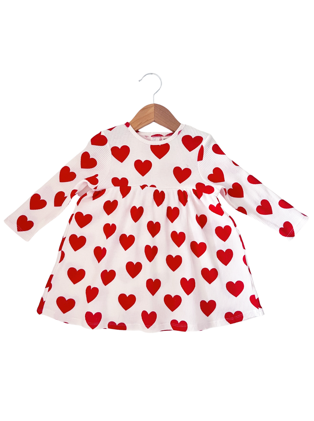 White long-sleeve dress with red heart patterns, hanging on a wooden hanger.