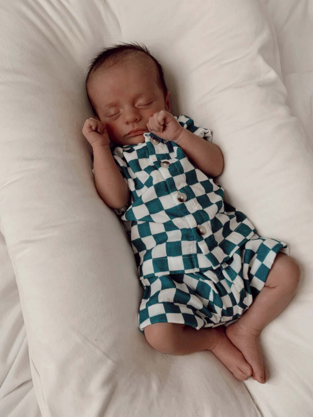 Baby boy sleeping on a soft pillow, wearing a turquoise and white checkered outfit.