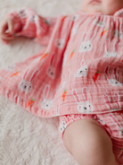 Baby wearing a pink outfit with bunny and carrot patterns, resting on a soft, textured blanket.