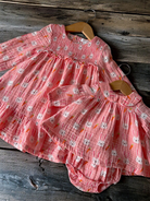 Two pink, bunny-patterned toddler dresses hanging on wooden hangers against a rustic wooden background.