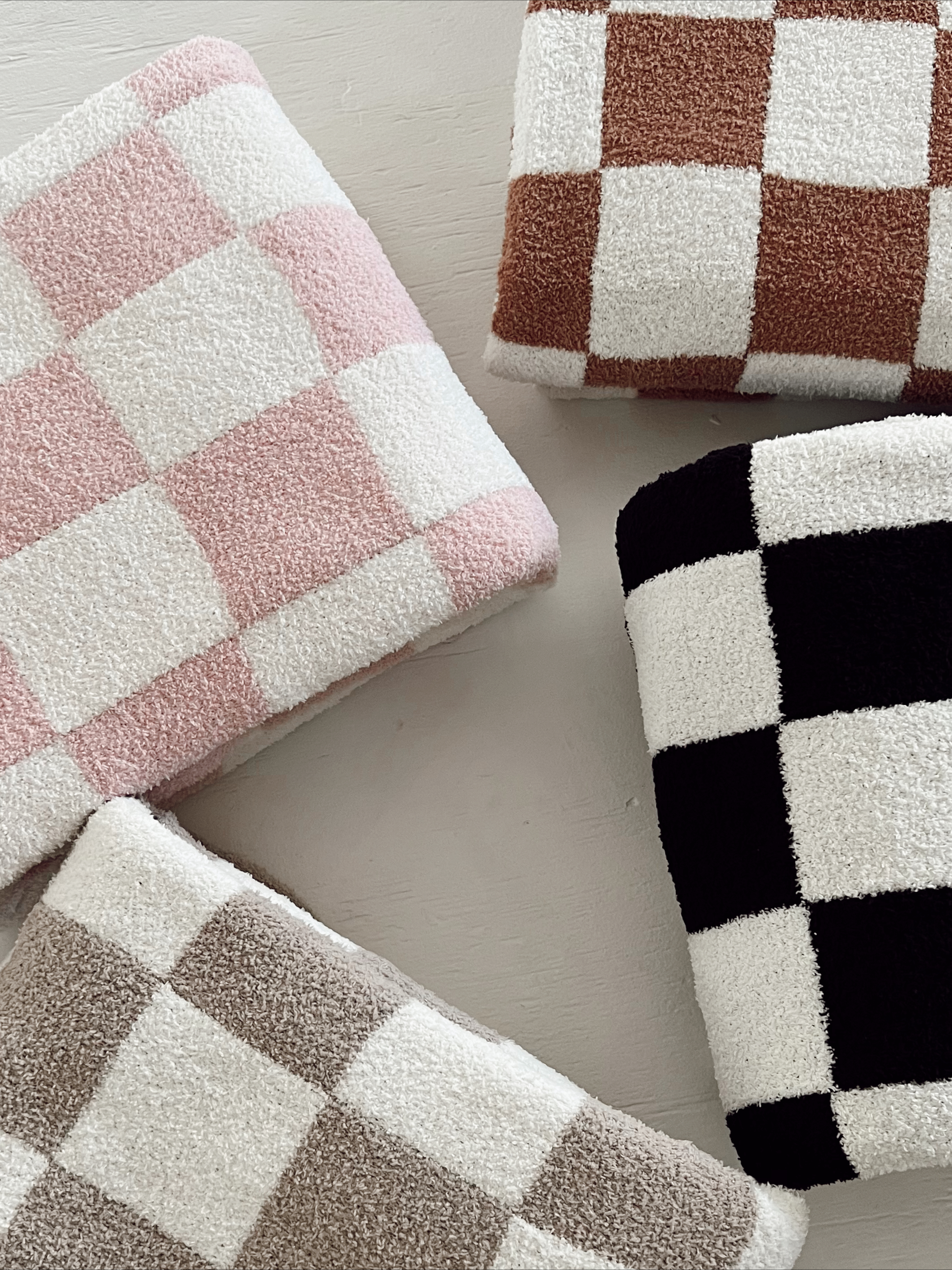 Four colorful checkered towels in pink, brown, tan, and black stacked on a light surface.