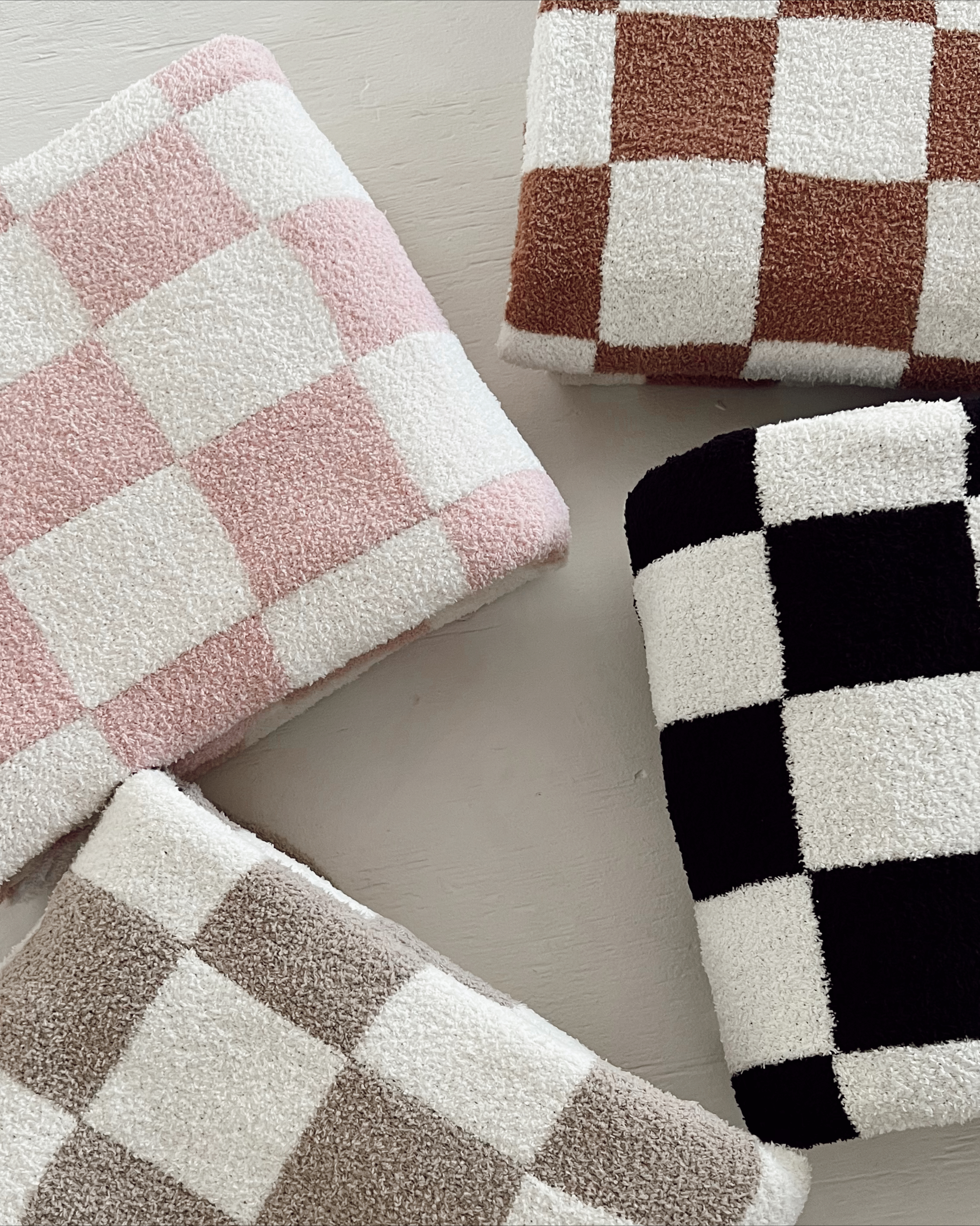 Four colorful checkered towels in pink, brown, tan, and black stacked on a light surface.