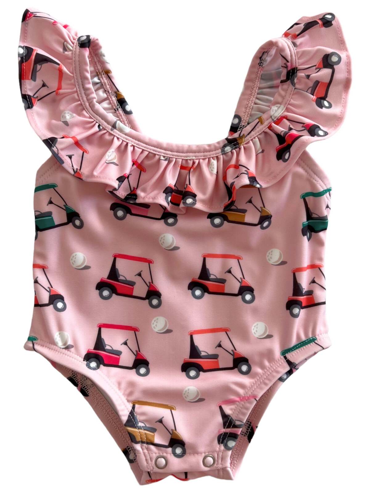 Pink one-piece swimsuit with golf cart and ball patterns, featuring ruffled shoulder straps.