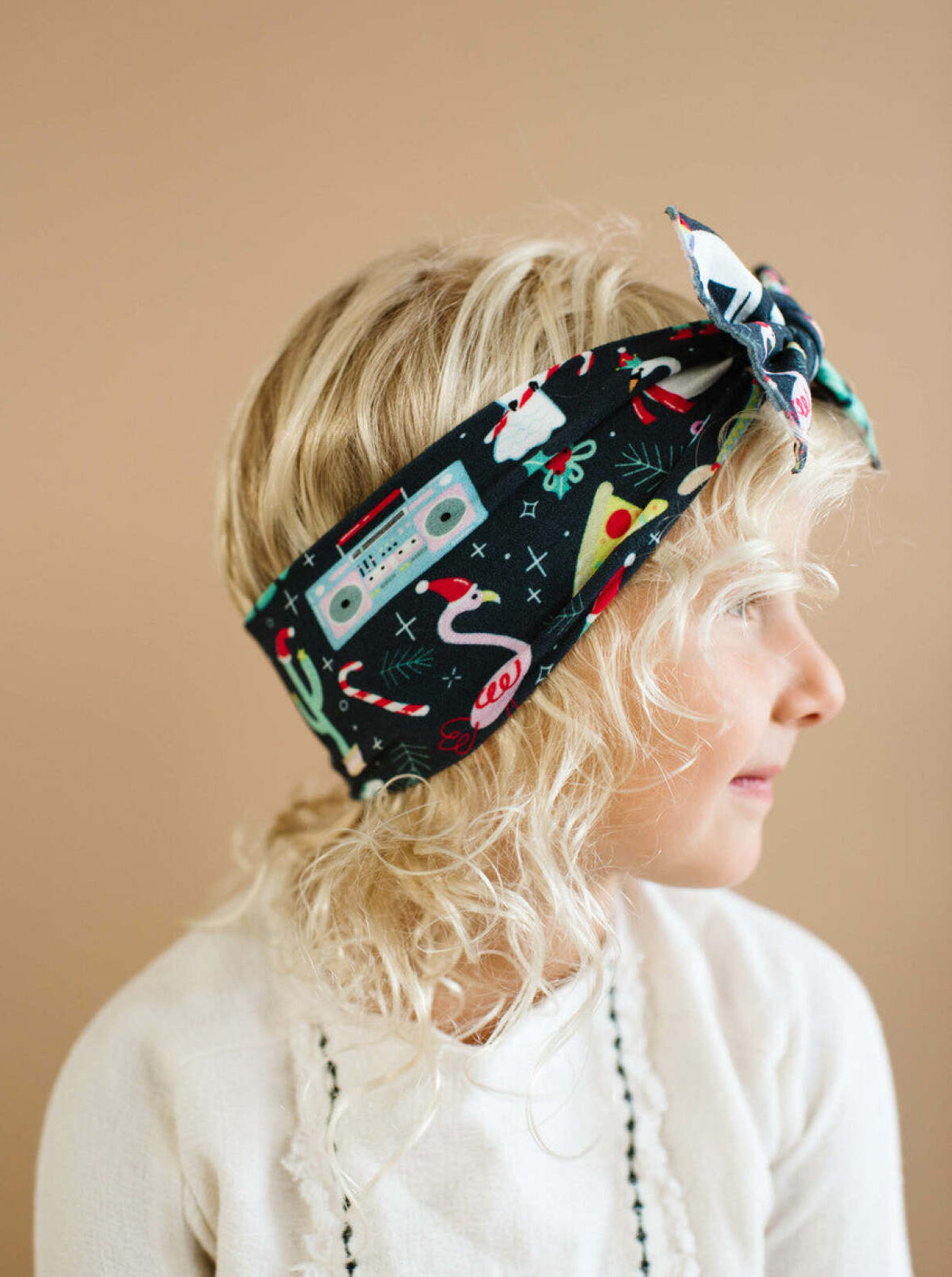 Child with curly blonde hair wearing a colorful patterned headband, side profile against a neutral background.
