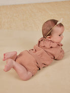 Baby wearing a pink outfit and headband, lying on their stomach on a soft surface.