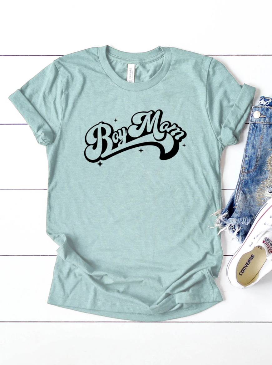 Light blue t-shirt with "Boy Mom" in bold black lettering, styled with denim shorts and white sneakers.