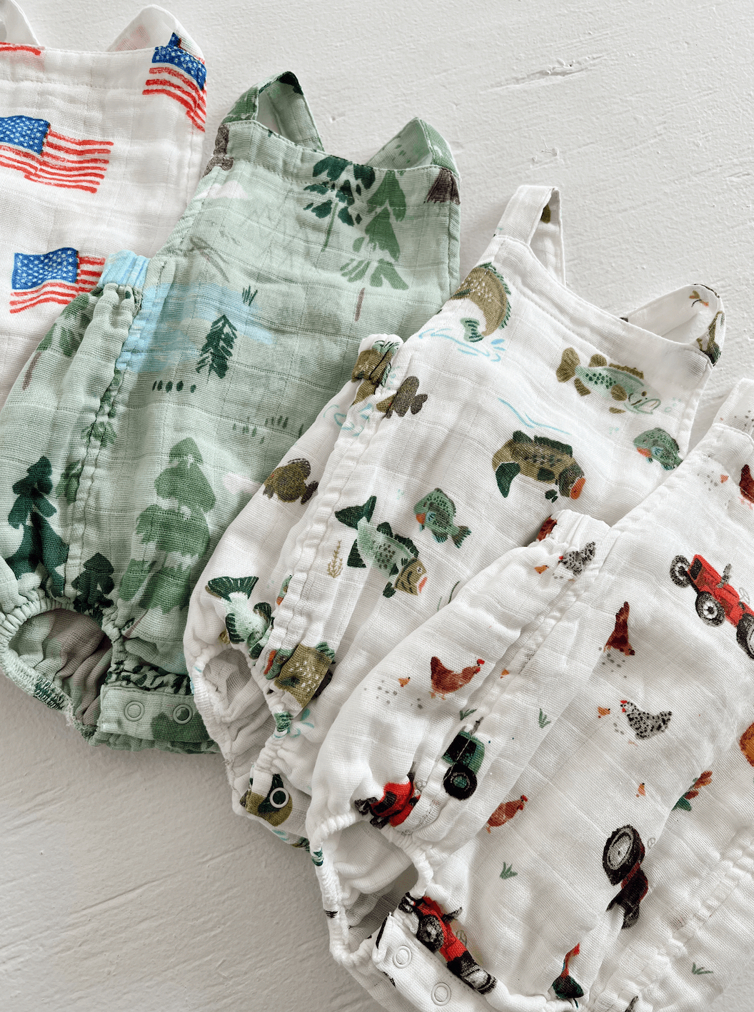 Four patterned baby rompers in green and white, featuring nature and farm themes.