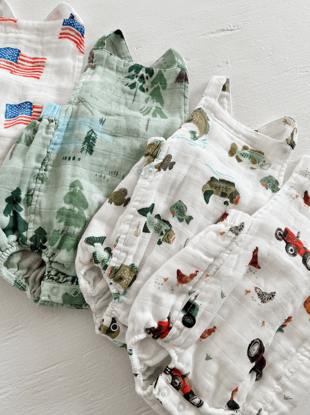 Four patterned baby rompers in green and white, featuring nature and farm themes.