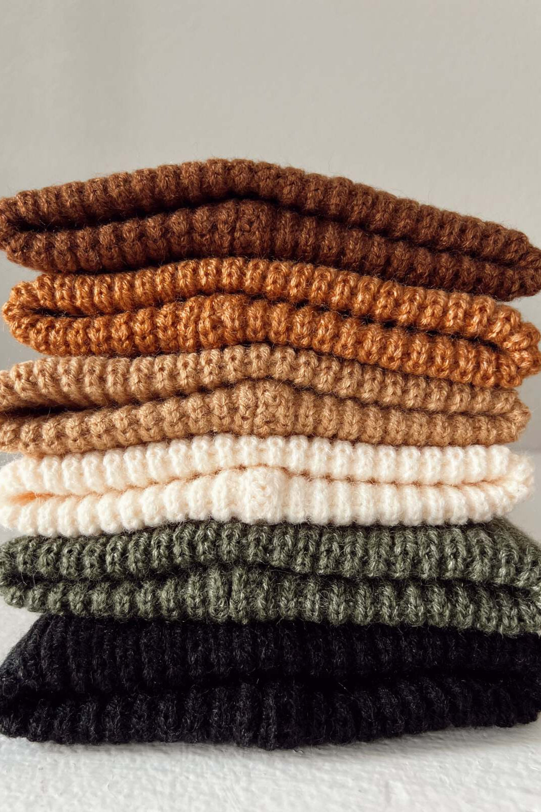 Stack of knitted fabric pieces in earthy tones: brown, orange, cream, green, and black, arranged neatly.