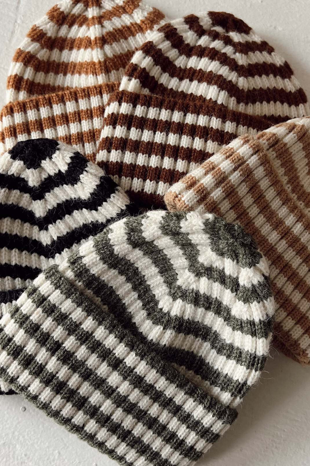 Collection of striped knit beanie hats in various colors, arranged together on a light background.
