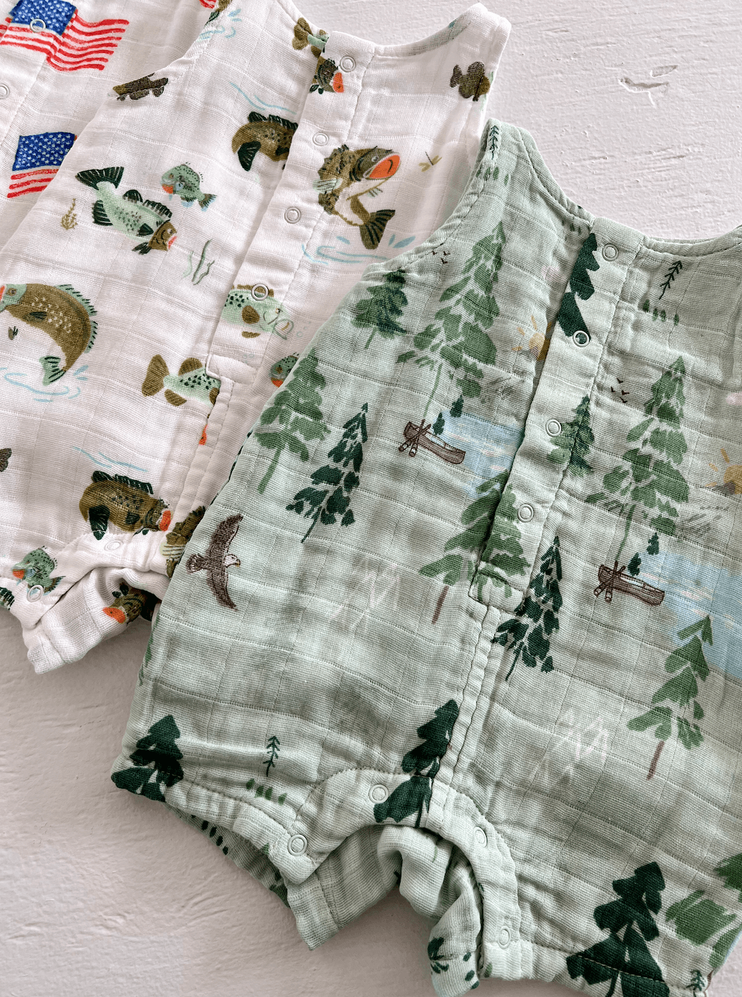 Three baby onesies with nature and fish prints in varying colors, laid out on a light background.