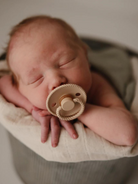 Newborn baby asleep in a soft blanket, holding a pacifier, with rosy cheeks and tiny hands visible.