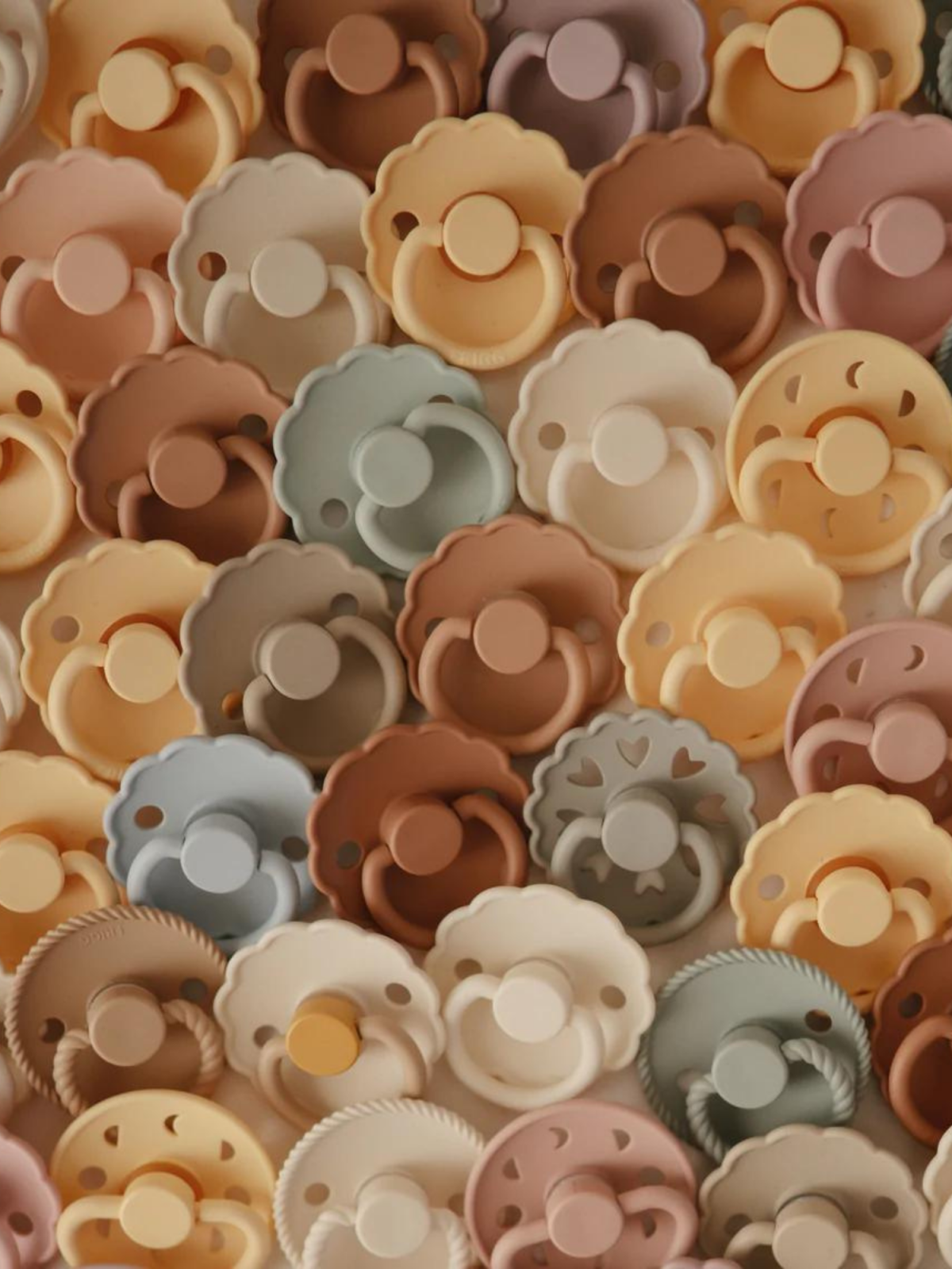 A colorful collection of baby pacifiers in various shapes and muted pastel tones.