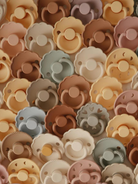 A colorful collection of baby pacifiers in various shapes and muted pastel tones.