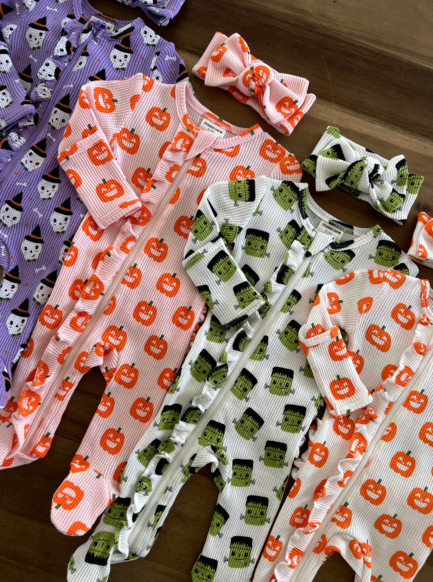 Colorful Halloween-themed baby rompers and headbands displayed on a wooden surface.