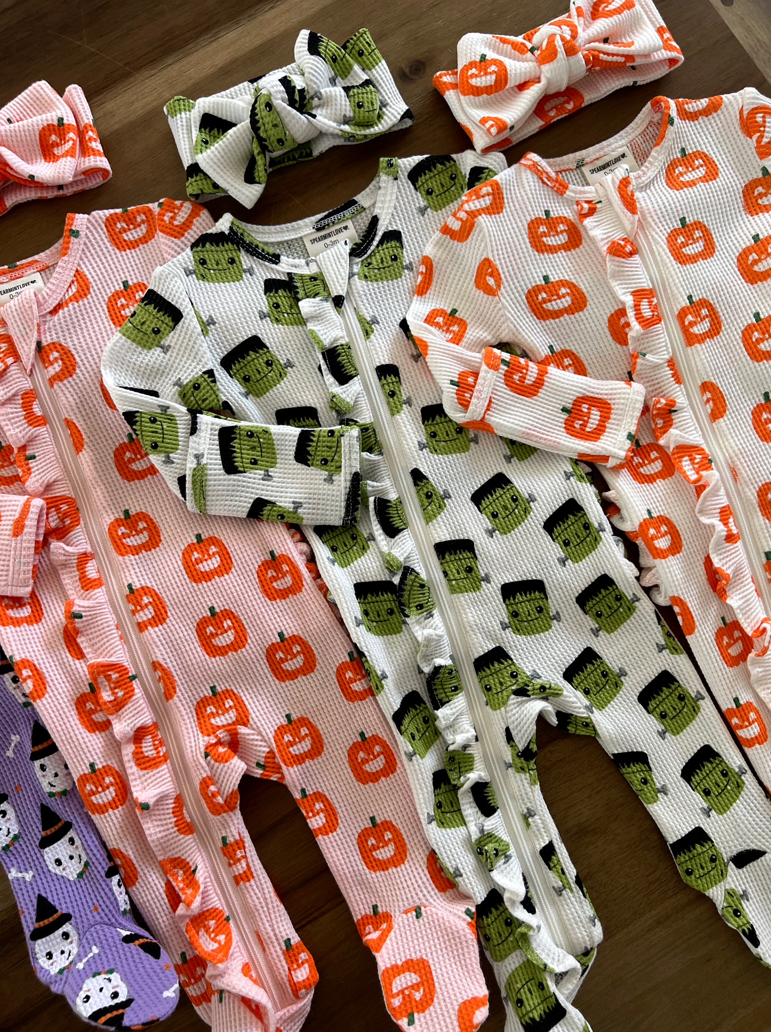 Colorful Halloween-themed toddler onesies with matching headbands featuring pumpkins and monsters.