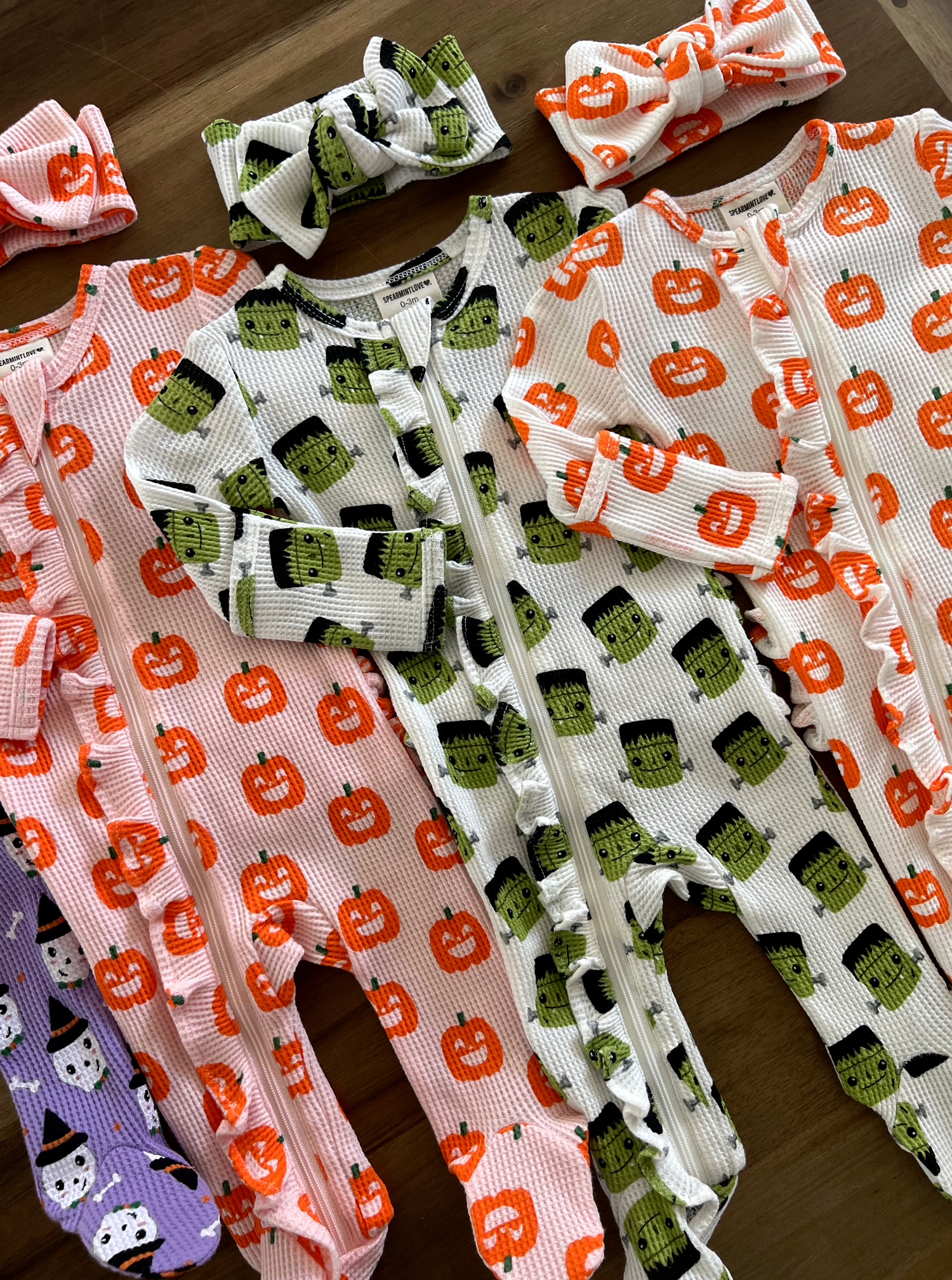 Colorful Halloween-themed toddler onesies with matching headbands featuring pumpkins and monsters.