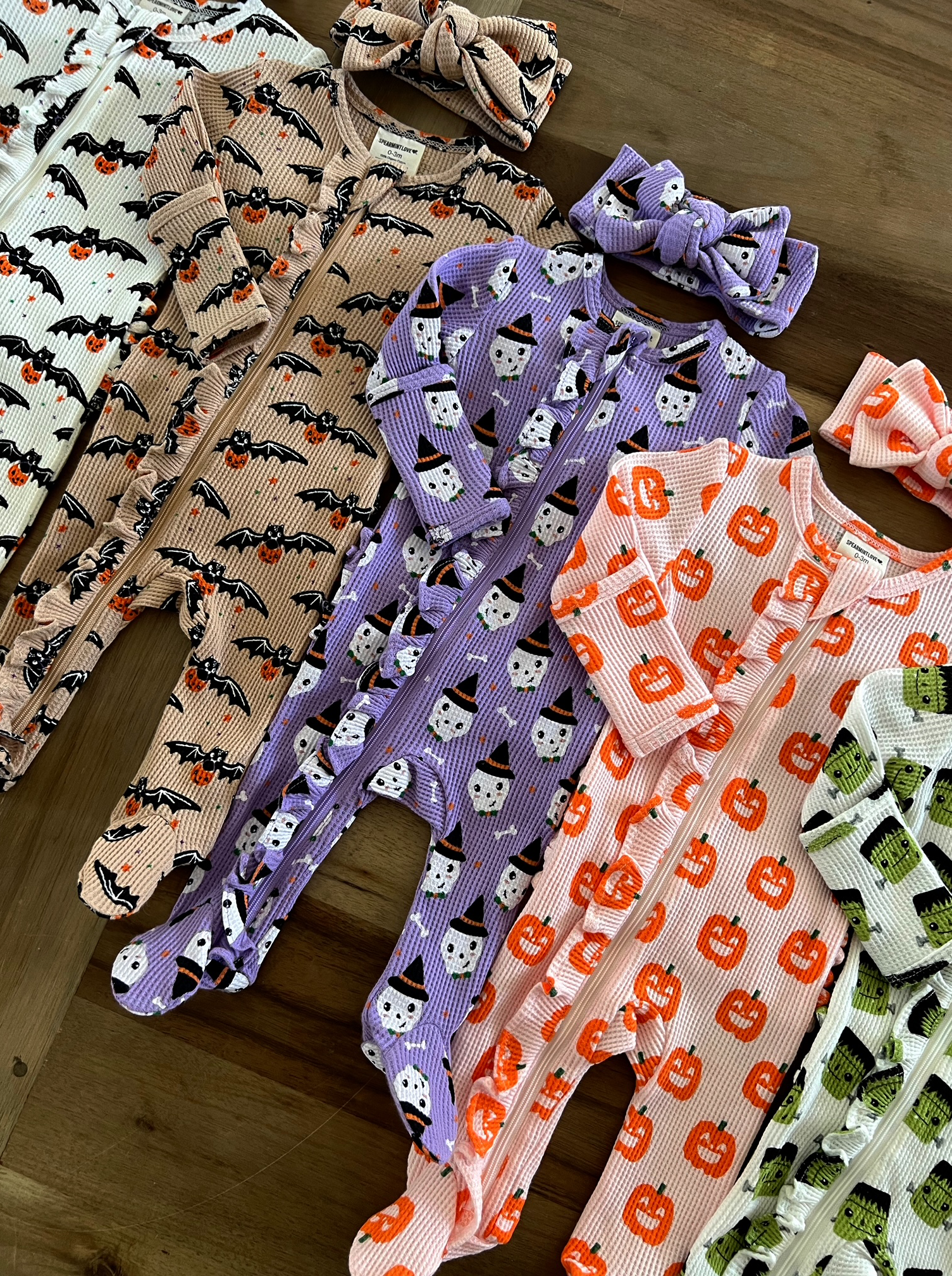Colorful Halloween-themed baby outfits and headbands in various patterns on a wooden surface.