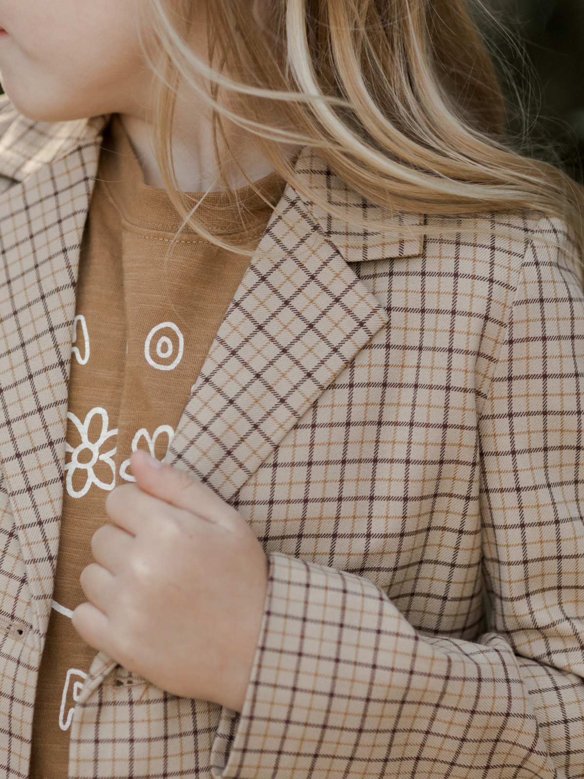 Child in a plaid blazer over a brown shirt with floral design, showcasing soft waves of hair.