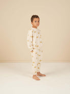 Young boy standing in a beige room, wearing light pajamas with a duck print, barefoot and looking at the camera.
