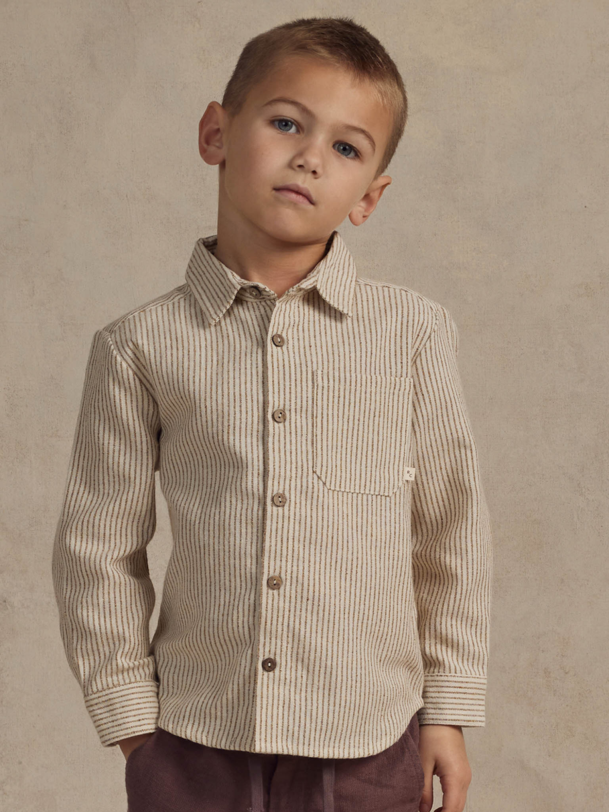 Child wearing a striped button-up shirt with a pocket, posing against a neutral background.