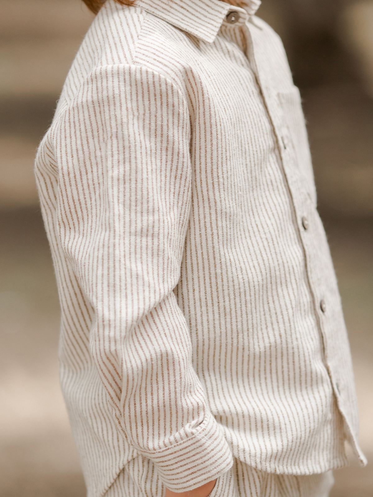 Child wearing a beige striped shirt, standing outdoors with a soft-focus background.