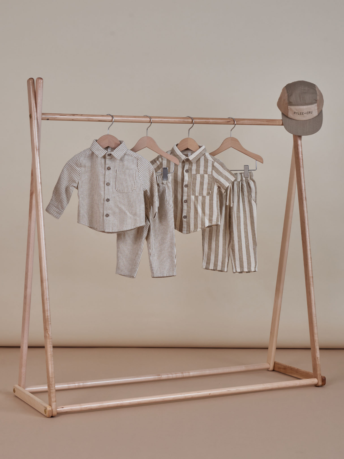 Children's striped clothing displayed on a wooden hanger stand with a matching cap overhead.