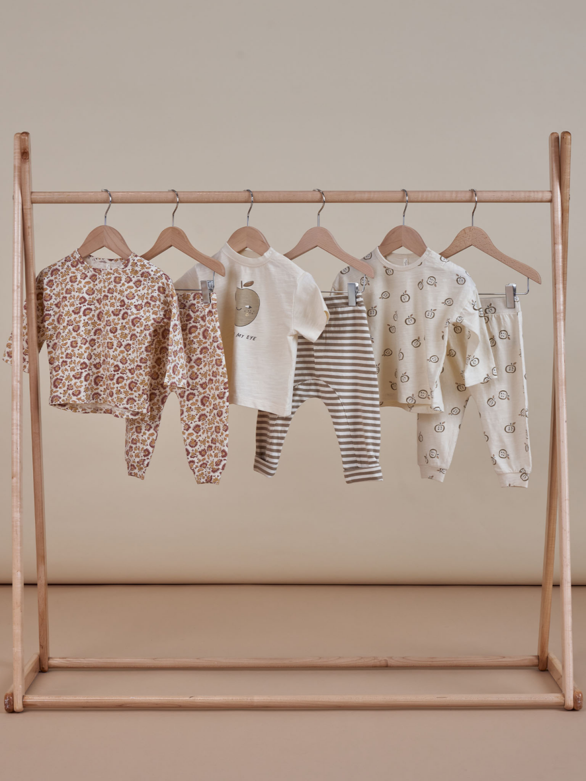 Baby clothes on a wooden rack: floral, striped, and patterned outfits in soft colors.