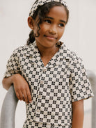Young girl in patterned outfit, smiling and leaning on a railing, wearing a matching headband.