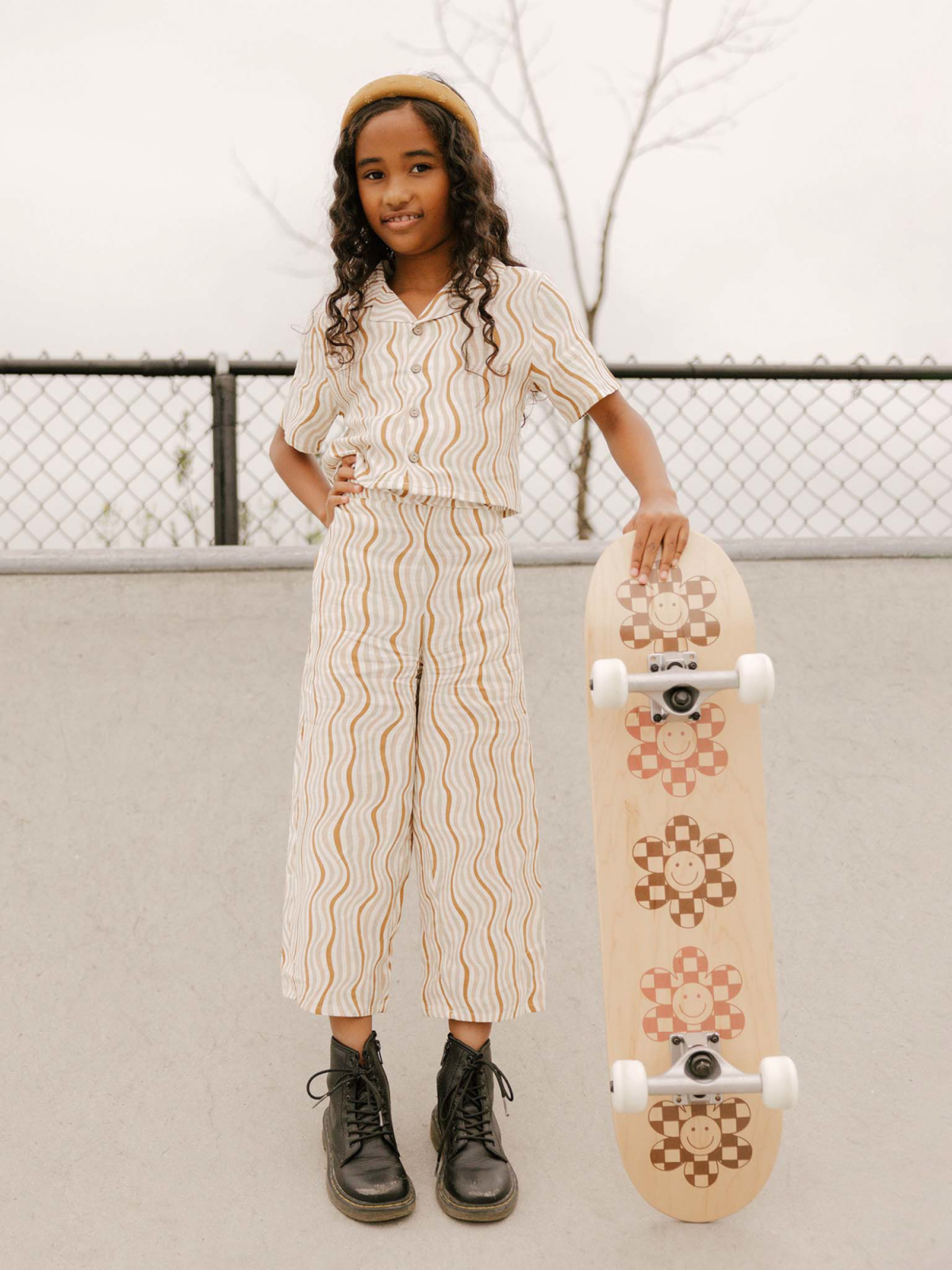 Girl in stylish outfit with skateboard, standing confidently at a skatepark.