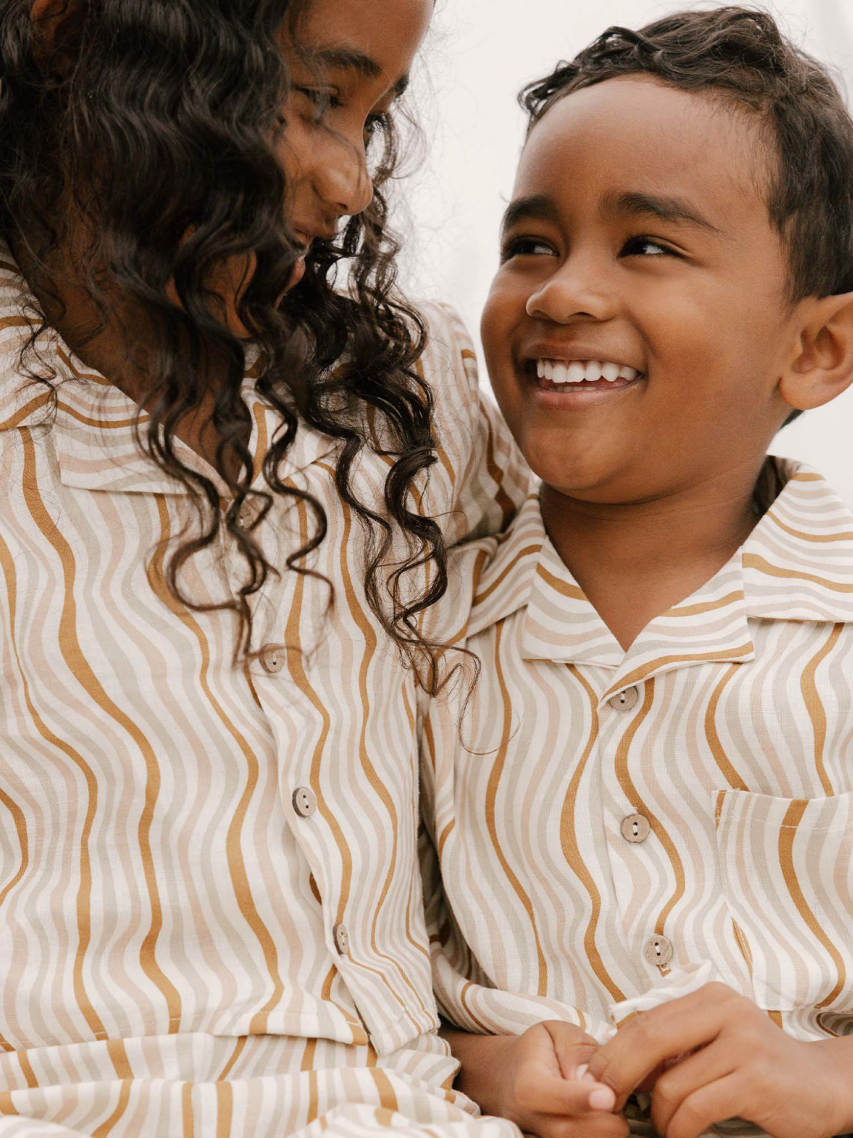 Two children in matching striped outfits share a joyful moment, smiling at each other.