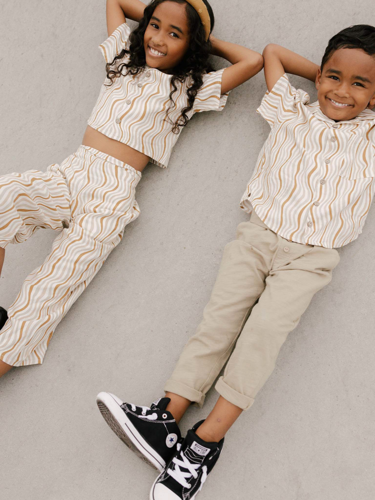 Two smiling children in matching striped outfits lie on the ground, enjoying a playful moment together.