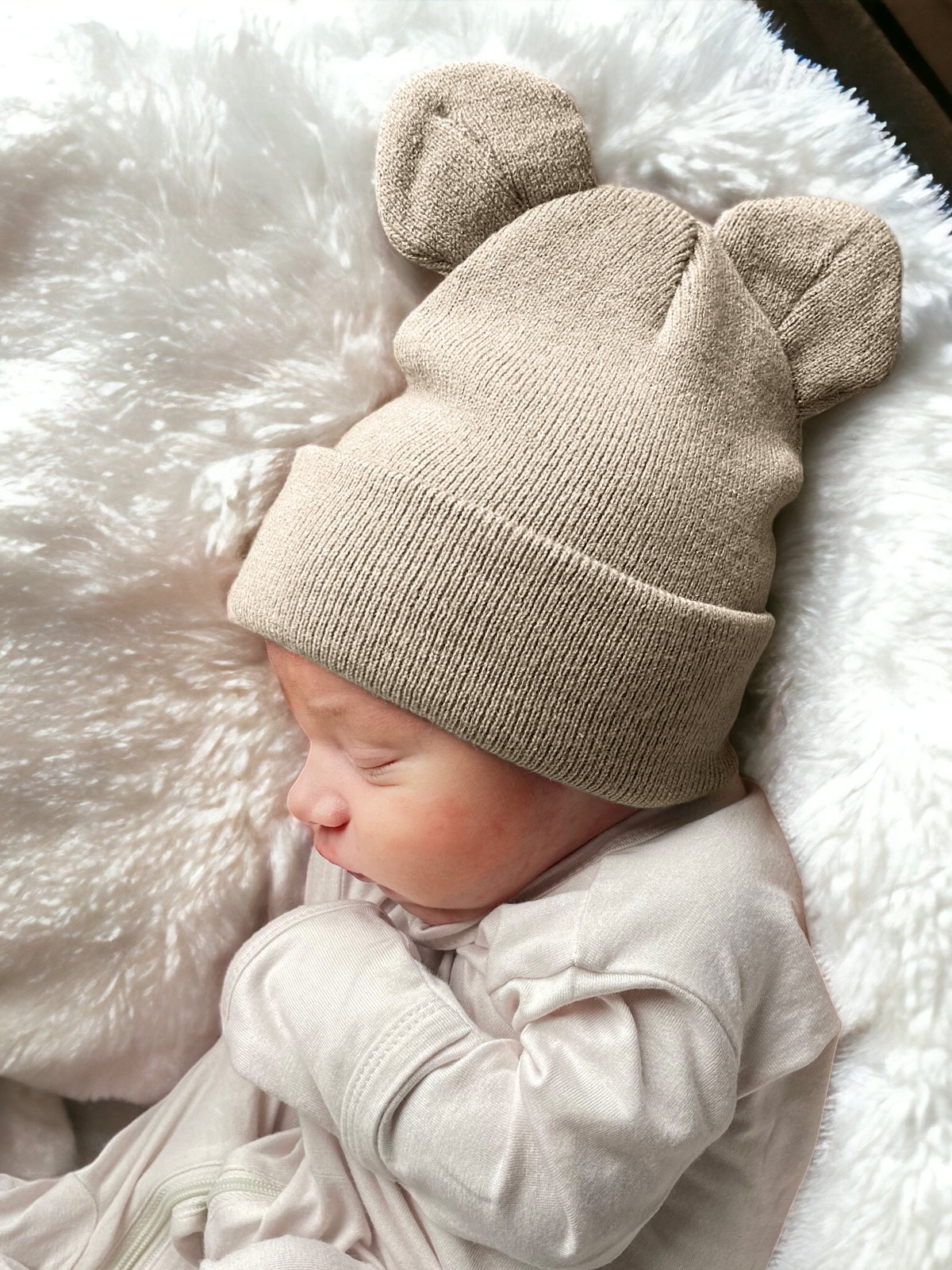 Baby sleeping on a fluffy blanket, wearing a beige knit hat with bear ears.