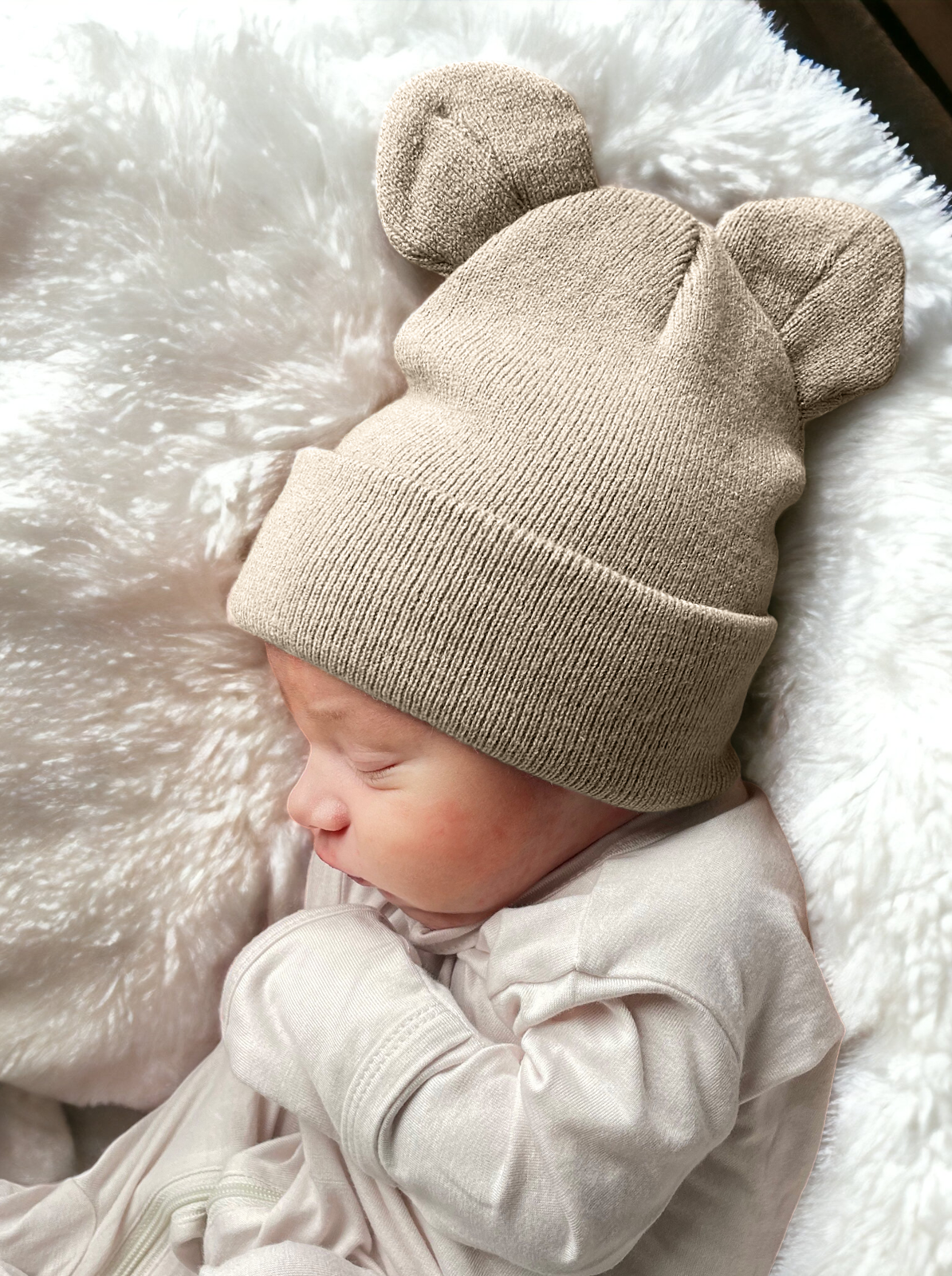 Baby sleeping on a fluffy blanket, wearing a beige knit hat with bear ears.