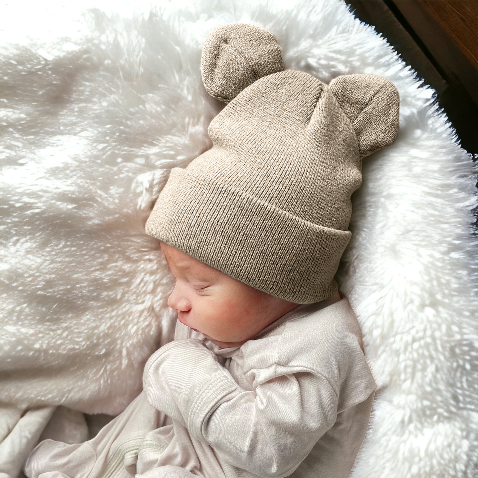 Baby sleeping on a fluffy blanket, wearing a beige knit hat with bear ears.
