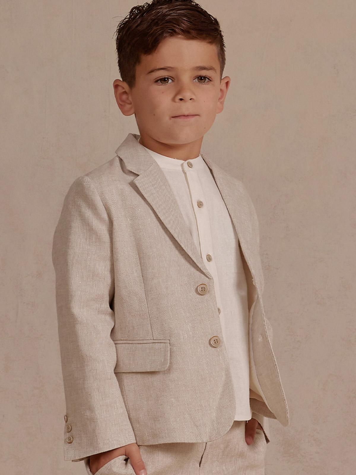 Young boy in a stylish light beige suit with a white shirt, standing confidently against a neutral background.