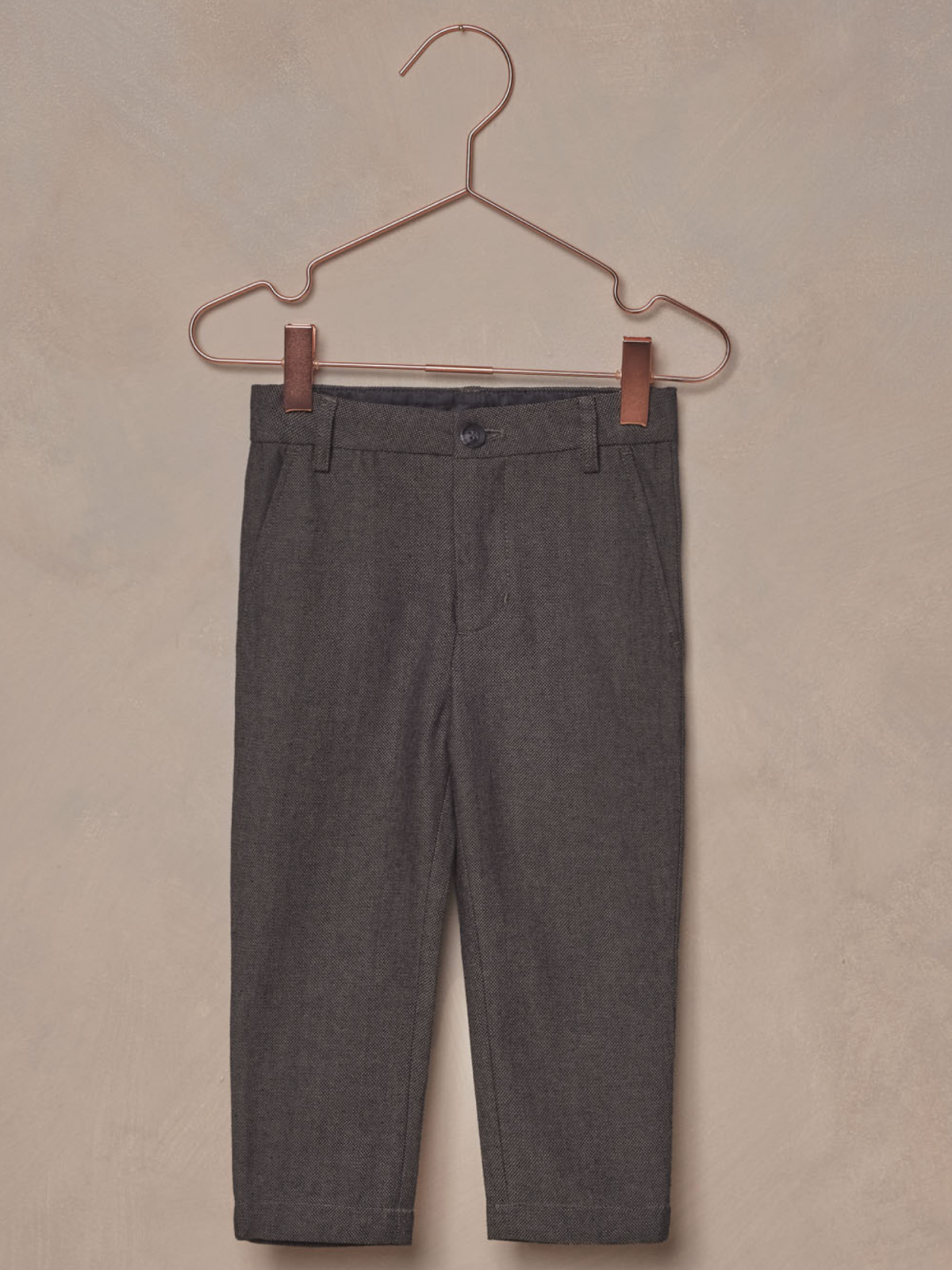 Gray toddler pants hanging on a copper hanger against a beige background.